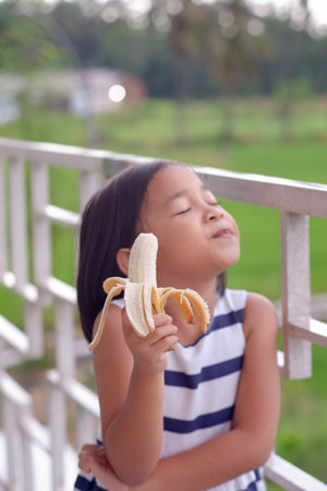 Portrait of cute little asian girl eat banana with nature backgroundの写真素材