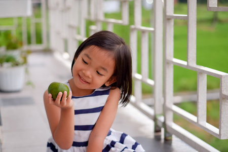 Little girl sitting on the balcony and holding a tangerineの写真素材