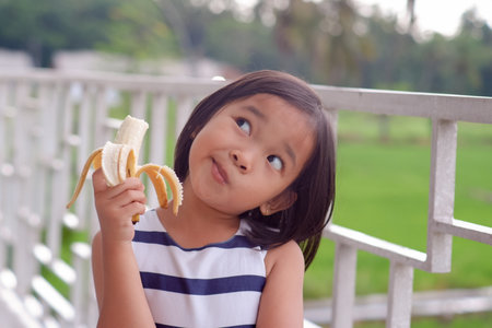 Portrait of cute little asian girl eat banana with nature backgroundの写真素材