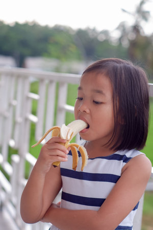 Portrait of cute little asian girl eat banana with nature backgroundの写真素材