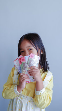 Asian young girl feel happy and holding some money of Indonesian rupiah. Concept of receiving THR on Eid al-Fitr or Lebaran days for muslim.の写真素材