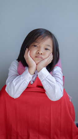 Little Asian girl in school uniform with a bored expression waiting for school hours to end or pick upの写真素材