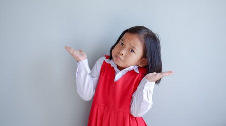 Asian child wearing school uniform with mouth full of food. i don't know gesture.の写真素材