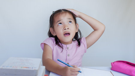 imaginative asian schoolgirl thinking while doing homework on the table.