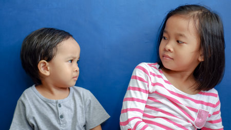 Portrait of two asian children looking at each other on blue backgroundの写真素材