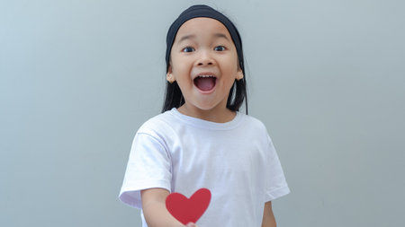 Happy asian little girl holding red paper heart on grey background.の写真素材