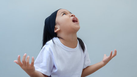 Little Asian girl kid wearing casual white tshirt crazy and mad shouting and yelling with aggressive expression and arms raised. frustration concept.の写真素材