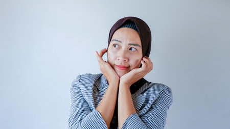 business woman wearing formal hijab keeps hands under chin thinking and glancing concept over gray...