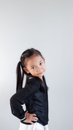 Side view of positive young Asian girl in black outfit smiling and looking at camera while standing...