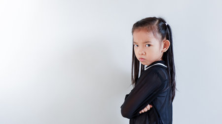 Young seven years old Asian girl in black dress isolated on a gray background. Angry, unhappy,...