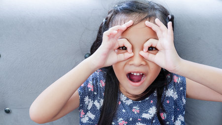 Young Asian girl over gray couch background doing ok gesture like binoculars, eyes looking through fingers.の写真素材