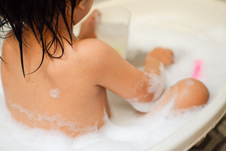 little Asian baby boy sitting in mini bath tub playing with toys in bathroom. Portrait of baby...