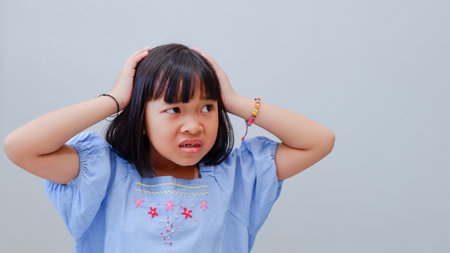 Frustrated cute Asian child girl wearing blue dress holding on forehead being depressed regretting what he did having headache, looking stressful.の写真素材