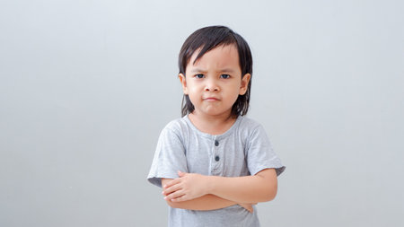 Asian boy toddler in grey shirt isolated on a gray background. Angry, unhappy, crossed hands, sad emotions on his face.の写真素材