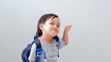 Cute Asian child student with backpack pointing with finger, funny gesture.の写真素材