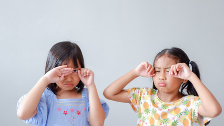 Two little girls sit with their faces hidden in their hands, appearing disappointed after a fight. The small preschooler children seem upset and hurt.の写真素材