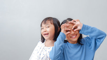 happiness friendship concept. Portrait of inquisitive little girls looking through fingers shaped like binoculars and expressing cheerful.の写真素材