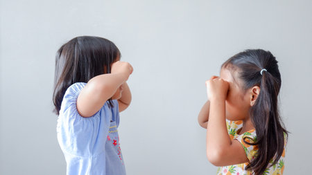 Two little girls sit with their faces hidden in their hands, feeling disappointed after a fight.の写真素材