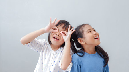 happiness friendship concept. Portrait of inquisitive little girls looking through fingers shaped like binoculars and expressing cheerful.の写真素材