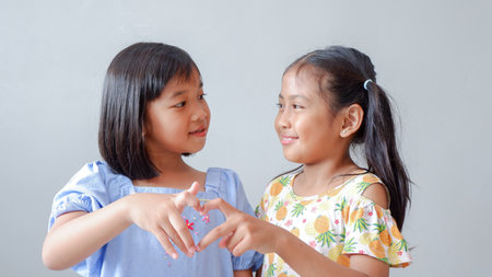 Cute little children with hearts finger sign on grey background. Friendship concept.の写真素材
