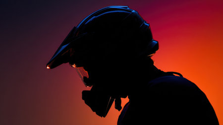 A striking silhouette of a motorbike rider wearing a helmet, set against a dynamic sunset blend of orange and purple hues, evokes a sense of adventure.の素材