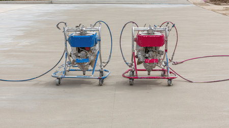 This image showcases two spray machines in blue and red, positioned on a freshly finished concrete surface, ideal for construction and renovation projects.の素材