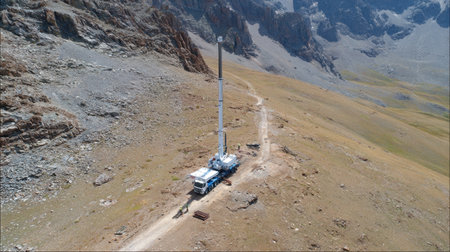 Aerial view of a communication tower installation on a remote mountain site, showcasing rugged terrain, a service vehicle, and expansive alpine scenery.の素材