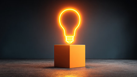 This striking image features an illuminated light bulb glowing in vibrant orange atop a cube, symbolizing creativity and inspiration in a modern environment.の素材
