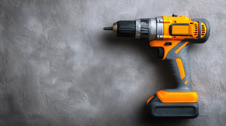 A bright orange cordless drill positioned on a smooth gray background, perfect for showcasing tools in home improvement or construction settings.の素材