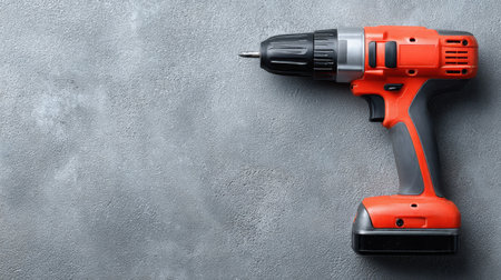 Close-up view of a cordless electric drill on a textured gray surface. Ideal for showcasing tools used in home improvement or DIY projects.の素材