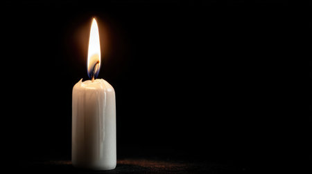 A solitary white candle burns brightly against a black background, casting a warm glow and creating a serene atmosphere perfect for relaxation or meditation.の素材