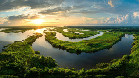 This stunning aerial view captures a winding river meandering through vibrant green marshland under a dramatic sunset sky, showcasing nature's tranquility.の素材