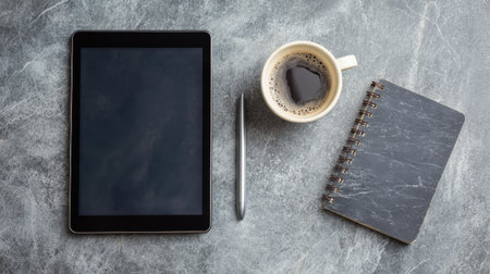 A sleek and modern workspace featuring a tablet, cup of coffee, pen, and a notebook on a textured grey background, ideal for creative professionals and inspiration.の素材