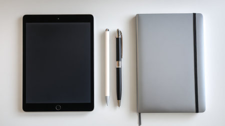 A sleek tablet, two pens, and a stylish notebook arranged neatly on a minimalistic desk, showcasing a modern workspace ideal for productivity and creativity.の素材