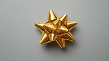 A striking golden decorative bow with sharp points rests against a neutral background, ideal for enhancing gift wrapping and creative craft projects.の素材