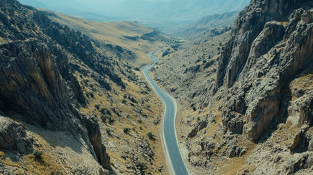 An enchanting aerial perspective captures a winding road snaking gracefully through rugged mountains, showcasing vast landscapes under a serene blue sky.の素材