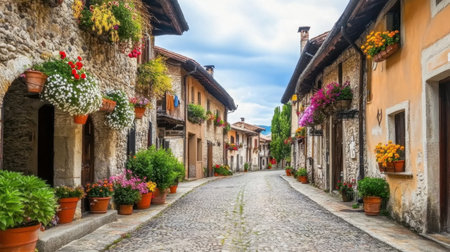 Discover a serene cobblestone street in a picturesque village, featuring charming stone buildings adorned with colorful flowers, set against a dramatic sky.の素材