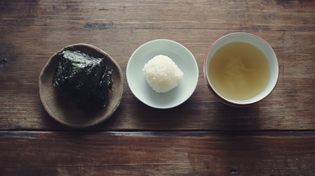 A visually appealing layout of a traditional Japanese meal featuring a rice ball, seaweed, and green tea presented on a rustic wooden table.の素材