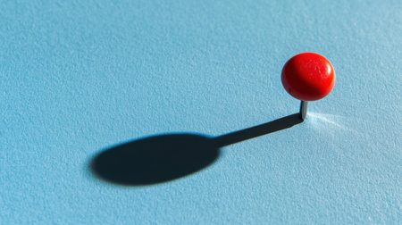 A vibrant red pushpin stands prominently on a light blue surface, casting a distinct shadow, showcasing minimalist design and appealing composition.の素材