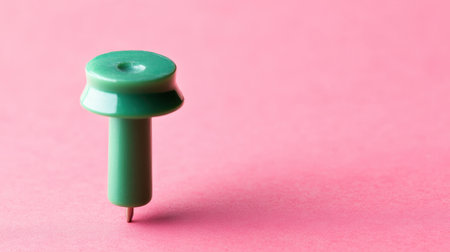 A vibrant green push pin stands prominently on a soft pink background, perfect for creative projects or office decor. This image captures simplicity and focus.の素材