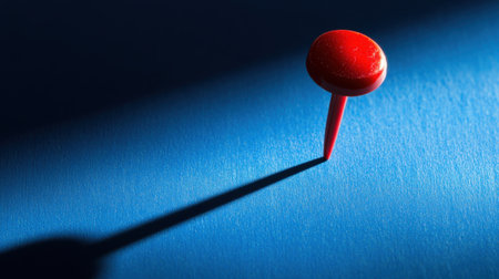This image showcases a striking red pushpin against a blue background, casting a long shadow that creates an intriguing visual contrast. Ideal for creative projects.の素材