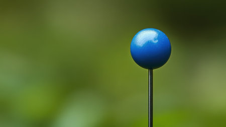 A vibrant blue pin stands tall on its slender metal point, set against a beautifully blurred green background that enhances its visual appeal.の素材