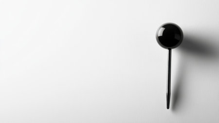 A sleek black push pin stands out on a minimalist white background, offering a modern perspective for office decor and organizing ideas.の素材