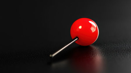 A vibrant red push pin rests elegantly on a dark, textured surface, showcasing its glossy finish and sharp point in an artistic close-up shot.の素材