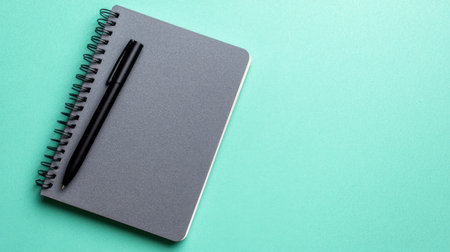 A stylish black spiral notebook paired with a sleek black pen placed on a vibrant mint green background, perfect for creative designs and inspiration.の素材