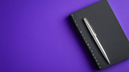 A sleek black notebook rests beside a silver pen, set against a vibrant purple background, ideal for creative writing, note-taking, or planning tasks.の素材