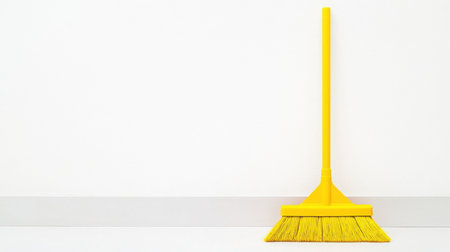 A bright yellow cleaning broom is positioned against a minimalist white wall, highlighting a sense of simplicity and cleanliness in modern interior spaces.の素材