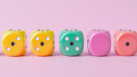 A lively display of colorful dice in yellow, green, pink, and blue, arranged in a row against a soft pink backdrop, perfect for playful themes.の素材