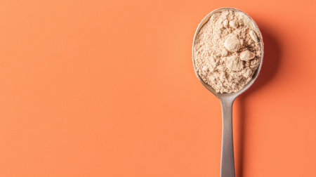 A close-up view of a metal spoon filled with light brown powder set against an orange background, ideal for culinary and health-related themes.の素材