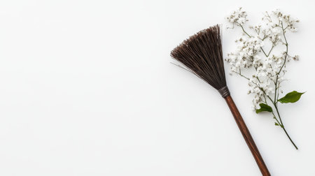 A rustic broom is artistically placed alongside delicate white flowers against a clean background, embodying a sense of simplicity and natural beauty in home decor.の素材